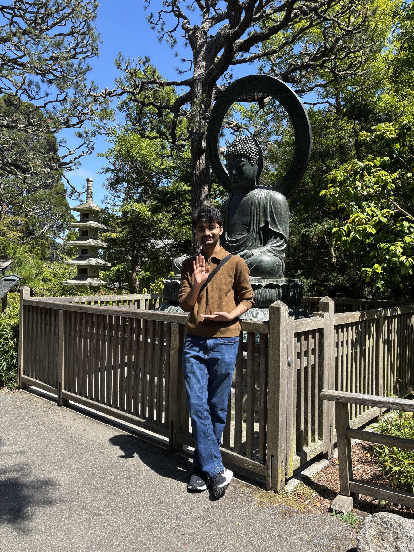 yash standing in front of a seated buddha statue surrounded by trees