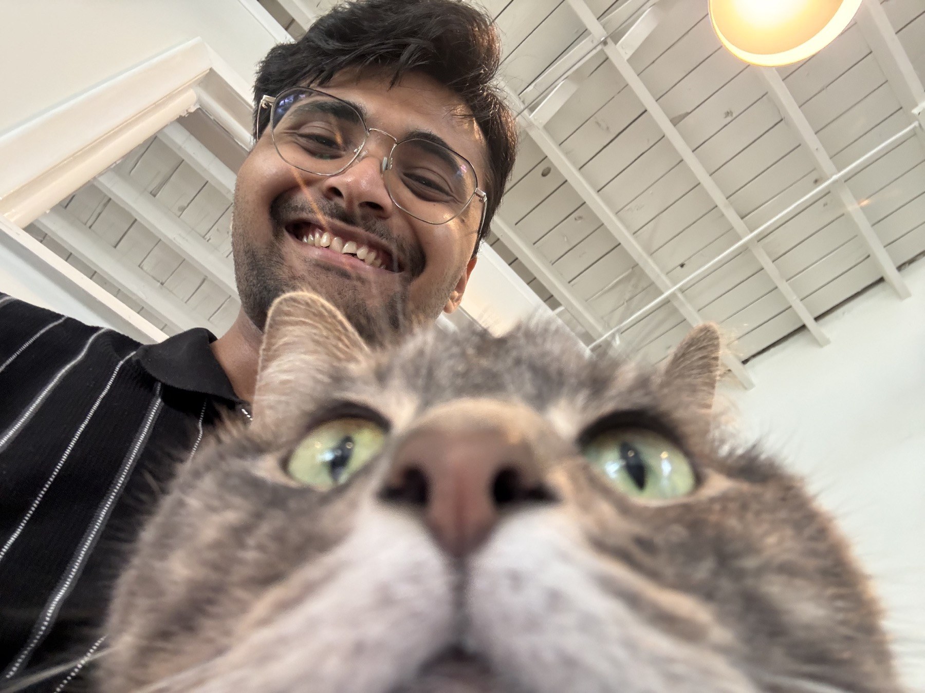 yash smiling behind a curious tabby cat close to the camera