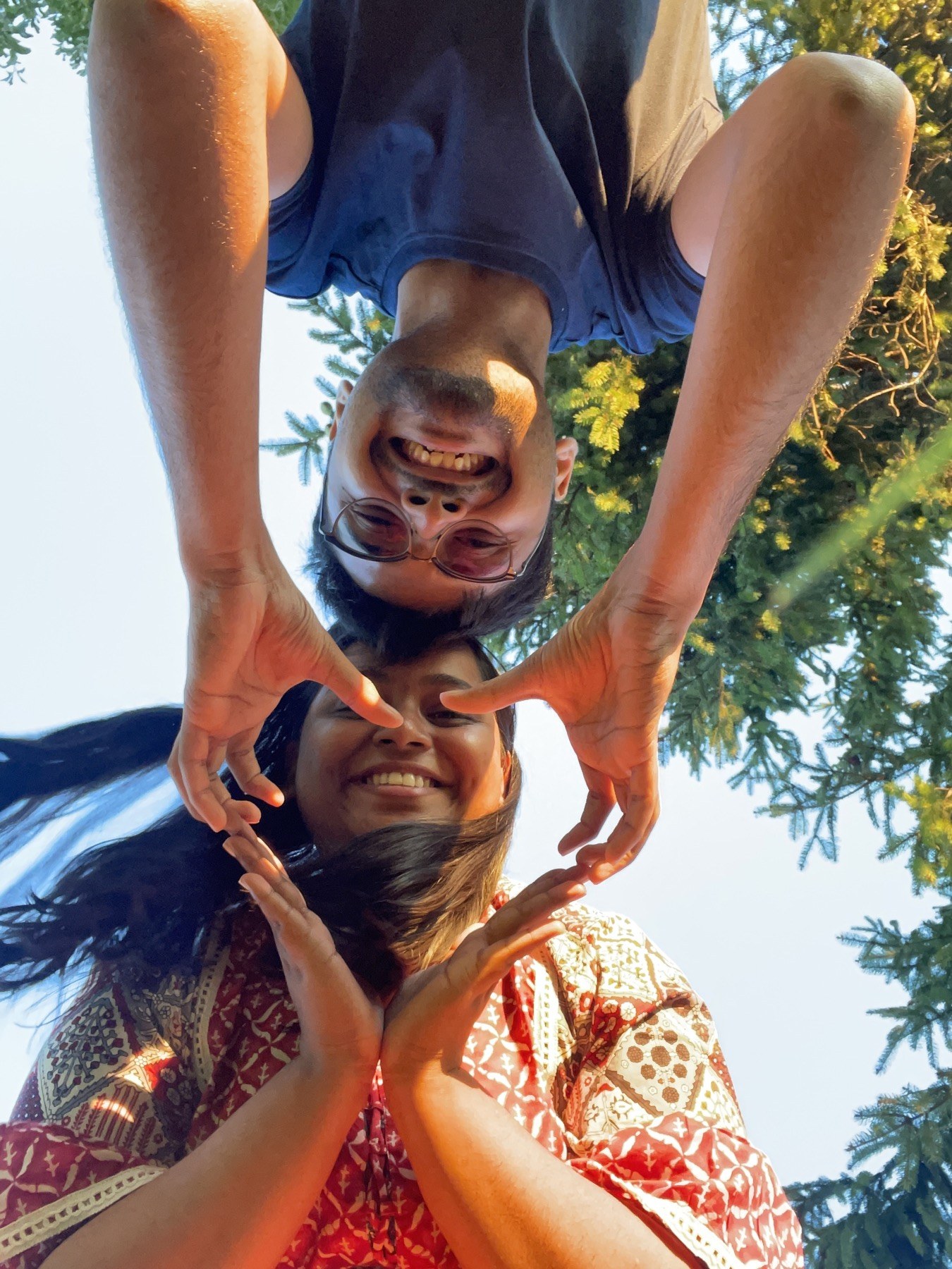 two people smiling at the camera and making a heart with their hands outdoors